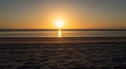 Obraz premium A tranquil beach scene showcases a vibrant sunset over calm waters. Sand in foreground