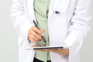 Close-up photo of female doctor wearing doctor's coat, stethoscope around neck, writing clinical notes, documents, patient list, insurance forms and prescriptions on tablet computer with tablet pen.
