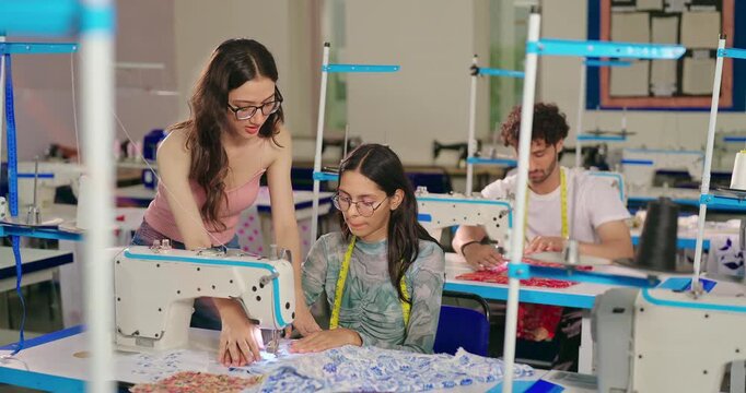 Indian young adult gen z woman lady wear tape around neck talk learn new clothe craft sewing course. Teen pupil girl female sitting desk help to stitch teach casual skill day indoor class room place