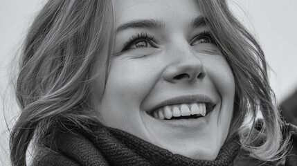 A black and white close up of a smiling, light-haired woman in a scarf, gazing upwards with a look of joyful optimism and anticipation.