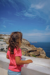 View of the Santorini seascape and distant islands, framed by a white railing and a young figure looking at the horizon.