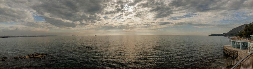ampia composizione panoramica con vista sul Golfo di Trieste, dalla costa vicino alla città, in primavera, di pomeriggio tardi, con mare calmo e cielo nuvoloso