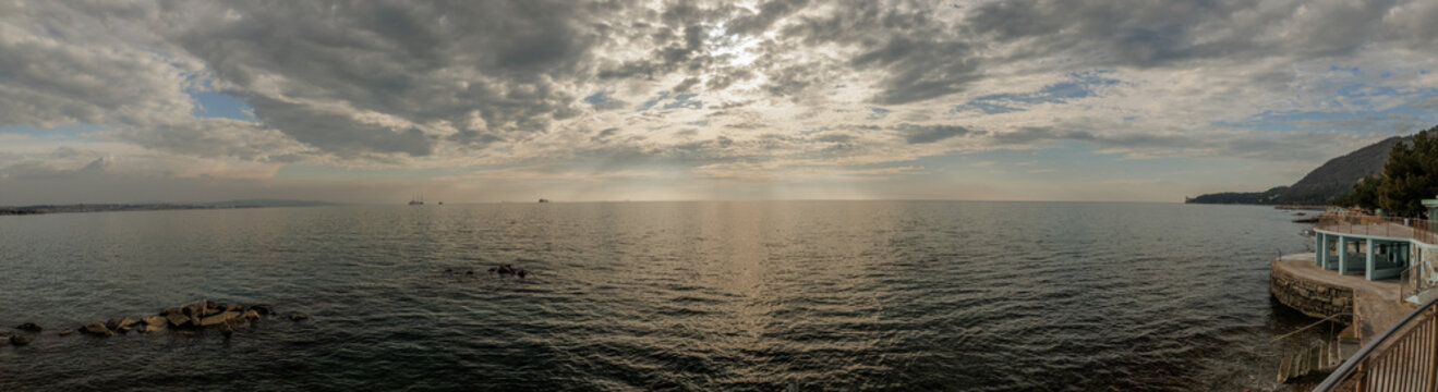 ampia composizione panoramica con vista sul Golfo di Trieste, dalla costa vicino alla citt&agrave;, in primavera, di pomeriggio tardi, con mare calmo e cielo nuvoloso
