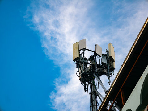 Cellular telecommunications tower with antennas and equipment against blue sky with white clouds and power lines