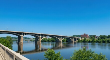 Fototapeta premium Concrete arch bridge spans a wide river, reflecting in the calm water under a clear blue sky