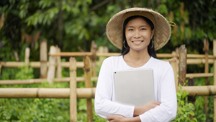 Southeast asian woman farmer smiling in vegetable garden or field with  a tablet in hands, looking...