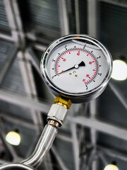 Pressure gauge displaying measurements in industrial setting with metal pipes and ceiling lights
