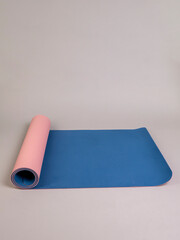 Double-sided pink and blue sports yoga mat in a half-open roll lies on a gray background