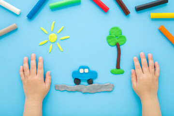 Little child boy hands making and creating car, tree and sun from colorful modeling clay on light blue table background. Pastel color. Closeup. Point of view shot. Top down view.