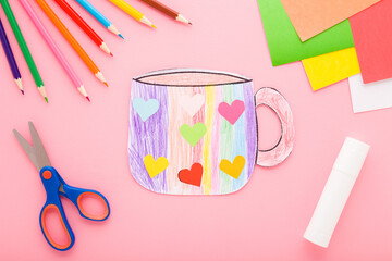 Paper mug shape painted with colorful pencils and glued with hearts. Kid handcraft on light pink...