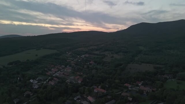 Aerial twilight view of F&uuml;z&eacute;r village in northern Hungary surrounded by forested hills and valleys at sunset, showing peaceful countryside scenery beneath a glowing evening sky.