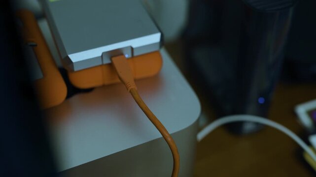 Moody macro closeup of a USB-C cable plugged into a mobile external drive stacked on a rugged LaCie beside another drive on a Mac Studio desktop, high angle, dramatic computer still life.