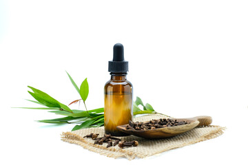 Clove essential oil in amber glass dropper bottles, dried clove spices on a wooden spoon, and natural herbal leaves arranged on a jute mat. Perfect for alternative medicine, herbal, skincare, wellness