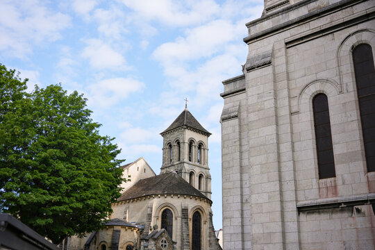 Old European stone buildings with arched windows and towers under a bright blue sky. Scenic city view with historical architecture and summer trees. - Powered by Adobe