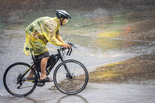 Cyclist in a raincoat rides through heavy rain on a city street