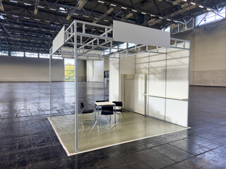 Weisser leerer Messestand in Messehalle mit schwarzen Stühlen und einem Tisch