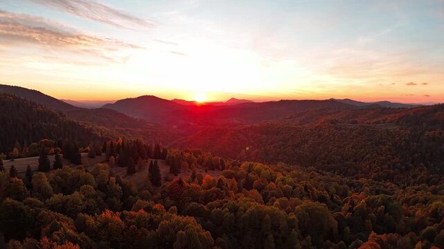 Aerial hyperlapse showing forward motion over colorful autumn mountain valley at sunset with glowing sky