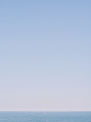 Distant Boat on Horizon Under Pale Blue Sky