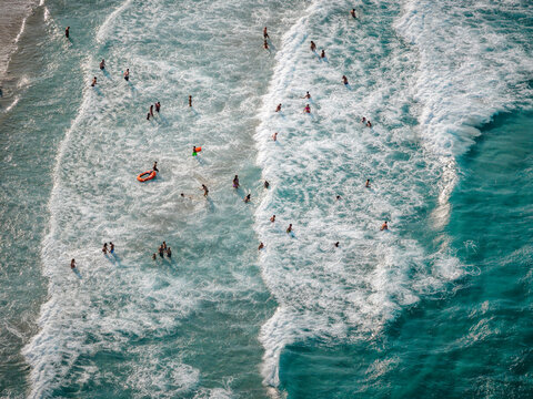Aerial view of the turquoise sea embracing the sandy shore, with people dotting the water like playful sprites, Torre dell'Orso, Apulia, Italy.