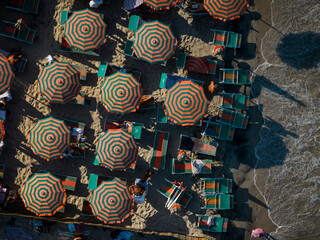 Aerial view of a sun-soaked beach with colorful umbrellas casting intricate shadows on the golden sand meeting the turquoise sea, Torre dell'Orso, Apulia, Italy.