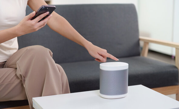 Smart Home. Woman using smartphone to control smart speaker in cozy living room. - Powered by Adobe