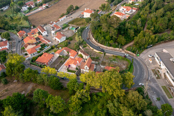 Drone view of curved road cutting through lush green landscape and residential village. Red roof houses, trees, and countryside scene highlight peaceful rural environment