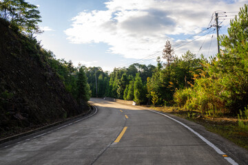 A Winding Road Through the Mountains Surrounded by Lush Greenery and Power Lines Under a Cloudy Sky