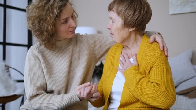 Concerned young daughter comforting her upset elderly mother, holding her hand and talking to her. Two generations sharing a moment of empathy, support, and care in a difficult situation