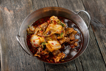 Sichuan lamb ribs with Chinese cabbage. Meat in an iron bowl on a wooden background. Chinese cuisine. Food concepts.