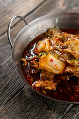 Sichuan lamb ribs with Chinese cabbage. Meat in an iron bowl on a wooden background. Chinese cuisine. Food concepts.