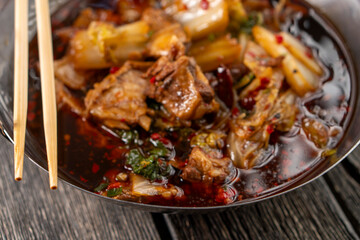 Sichuan lamb ribs with Chinese cabbage. Meat in an iron bowl on a wooden background. Chinese cuisine. Food concepts.