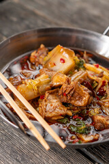 Sichuan lamb ribs with Chinese cabbage. Meat in an iron bowl on a wooden background. Chinese cuisine. Food concepts.