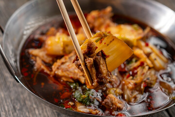 Sichuan lamb ribs with Chinese cabbage. Meat in an iron bowl on a wooden background. Chinese cuisine. Food concepts.