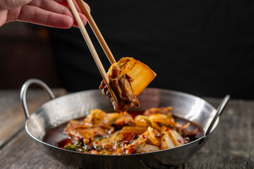 Sichuan lamb ribs with Chinese cabbage. Meat in an iron bowl on a wooden background. Chinese...