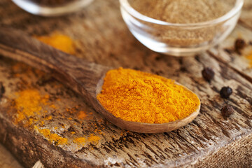 Turmeric root powder on a spoon with ground and whole black pepper in the background