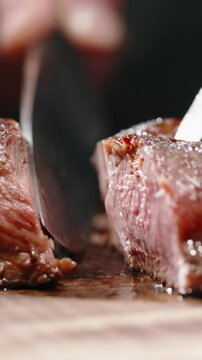 Vertical slow motion video knife cutting grilled beef steak medium well doneness juicy meat close up cinematic lighting gourmet restaurant concept fine dining premium food dark background macro detail