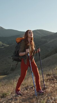 red haired woman hiking alone in autumn mountains with backpack and trekking poles vertical slow motion video symbolizing freedom mindfulness adventure lifestyle and solo travel spirit