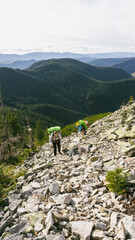 Fototapeta premium A group of tourists walking along a rocky ridge, over large stones in the mountains, hiking with large backpacks, travel and adventure, views of the peaks, beautiful landscapes. 
