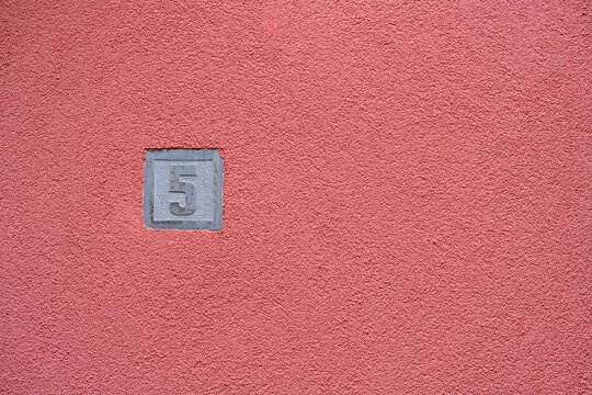 Number 5 embossed on textured pink stucco wall. Embossed house number 5 finding on a vibrant pink stucco wall texture.