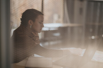 A woman is focused on her work at a desk in a serene office setting. The blurred foreground adds an...