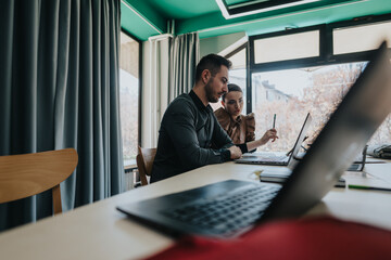 A man and woman working together on laptops, discussing ideas in a bright, contemporary office.