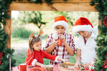 Happy children preparing for Christmas. Two boys and girl in santa hat, color gingerbread cookies outside having fun. kids decorate gingerbread man. homemade Christmas cookies. Holidays concept