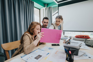 Three coworkers engaged in teamwork, working together on a project using a pink tablet and...
