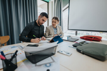 Two colleagues collaborating in a modern workspace, surrounded by office tools and materials.