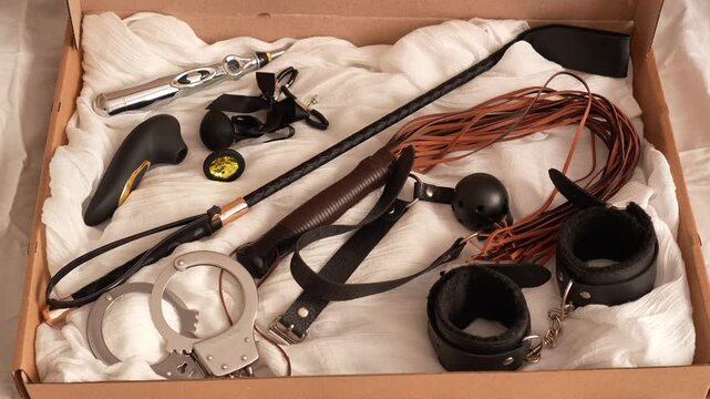 Woman in black transparent glove opens box with black adult toys. BDSM erotic set. Adult toys. Whip, gag, handcuffs, vacuum vibrator, butt plug, nipple clamps, electric stimulator