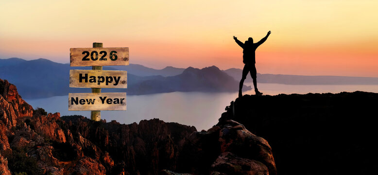 2026 hapy new year written on wooden post sign and silhouette of hiker with their arms up on a cliiff in seascape in front of sunset