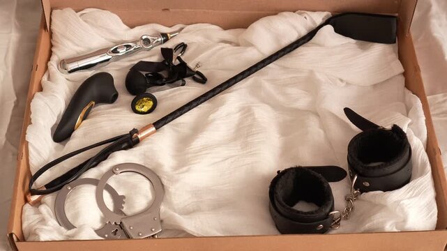 Woman in black transparent glove takes adult toys from box. BDSM erotic set. Adult toys. Whip, gag, handcuffs, vacuum vibrator, butt plug, nipple clamps, electric stimulator
