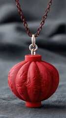 Detailed Product Style Photo of a Glittering Red Lantern Shaped Pendant Necklace with Intricate Carvings Suspended Against a Textured Gray Fabric Background with Subtle Lighting