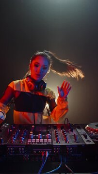 Vibrant slow motion vertical video of Asian woman DJ smiling and dancing behind console, creative artist enjoying nightlife rhythm, expressing happiness, connection and unity through music