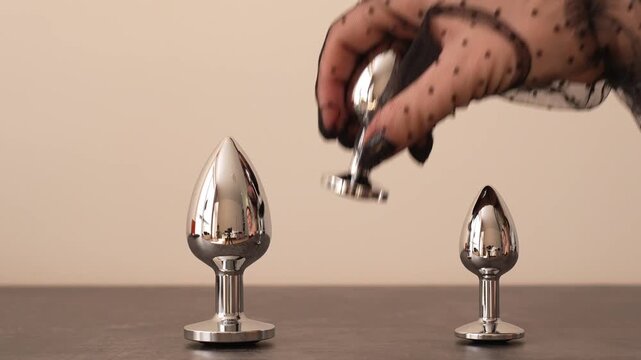 A woman in a black transparent glove reaches out and takes a metal anal plug with a black crystal from the shelf. BDSM erotic set. Adult toys.